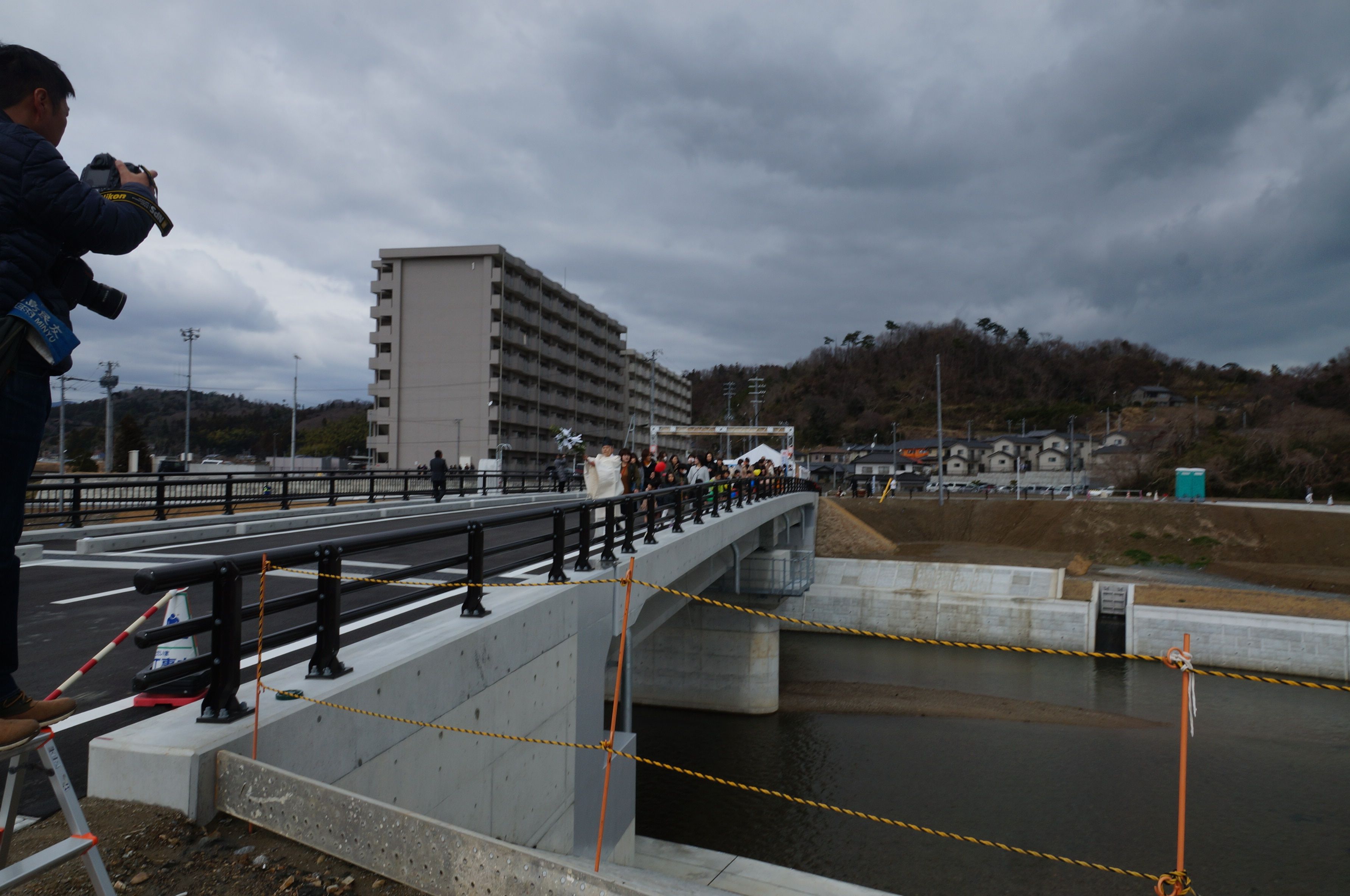 コンクリート橋として完成した代ノ下橋の渡り初め 遠方に見えるのは、災害公営住宅「市営久之浜東団地」。〔平成30(2018)年3月、いわきジャーナル撮影〕