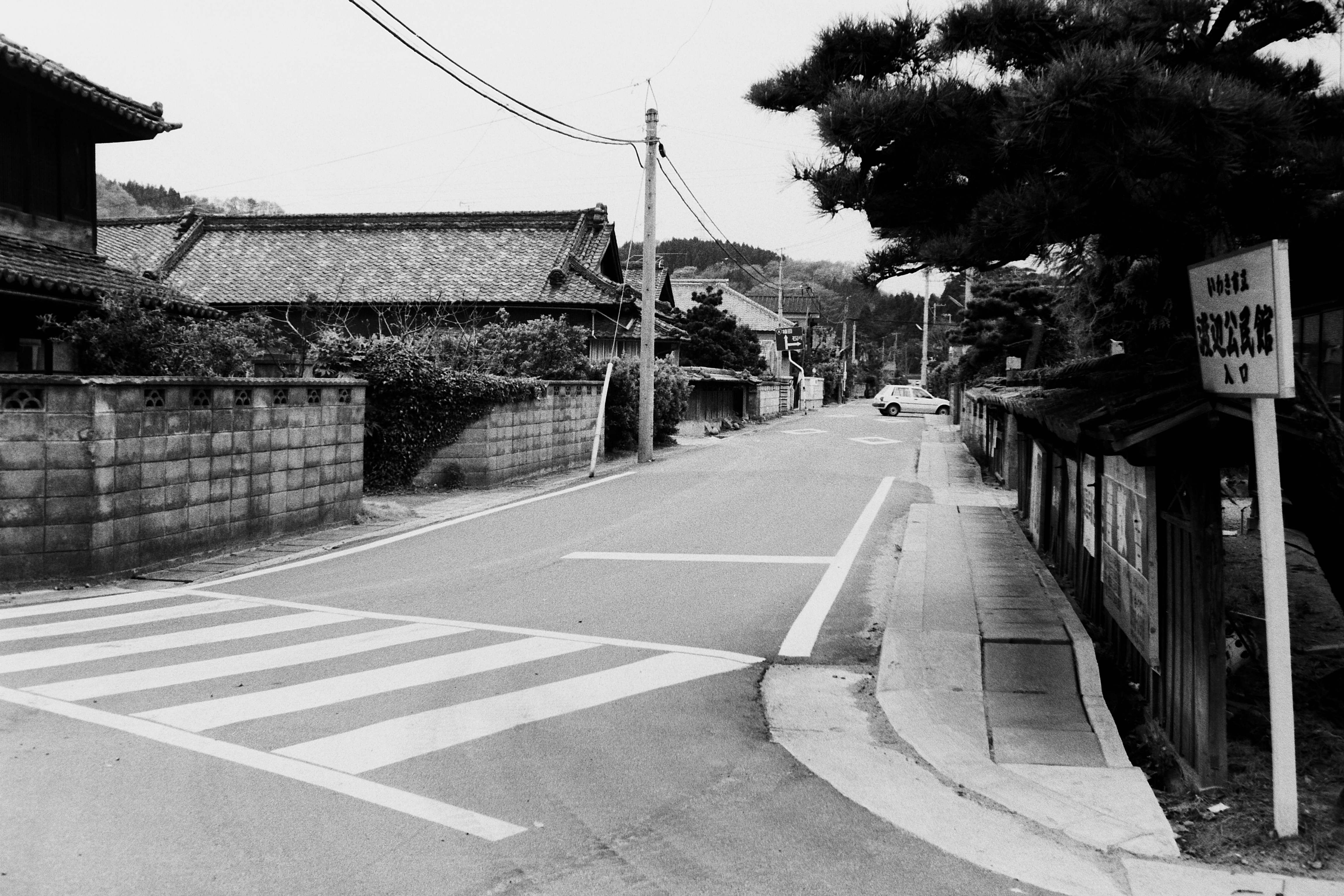 渡辺公民館入口から南方を見る。写真左に見える建物が旧角屋、自動車が見えるのは、釡戸に至る分岐点　(昭和62年5月、高萩純一氏撮影)