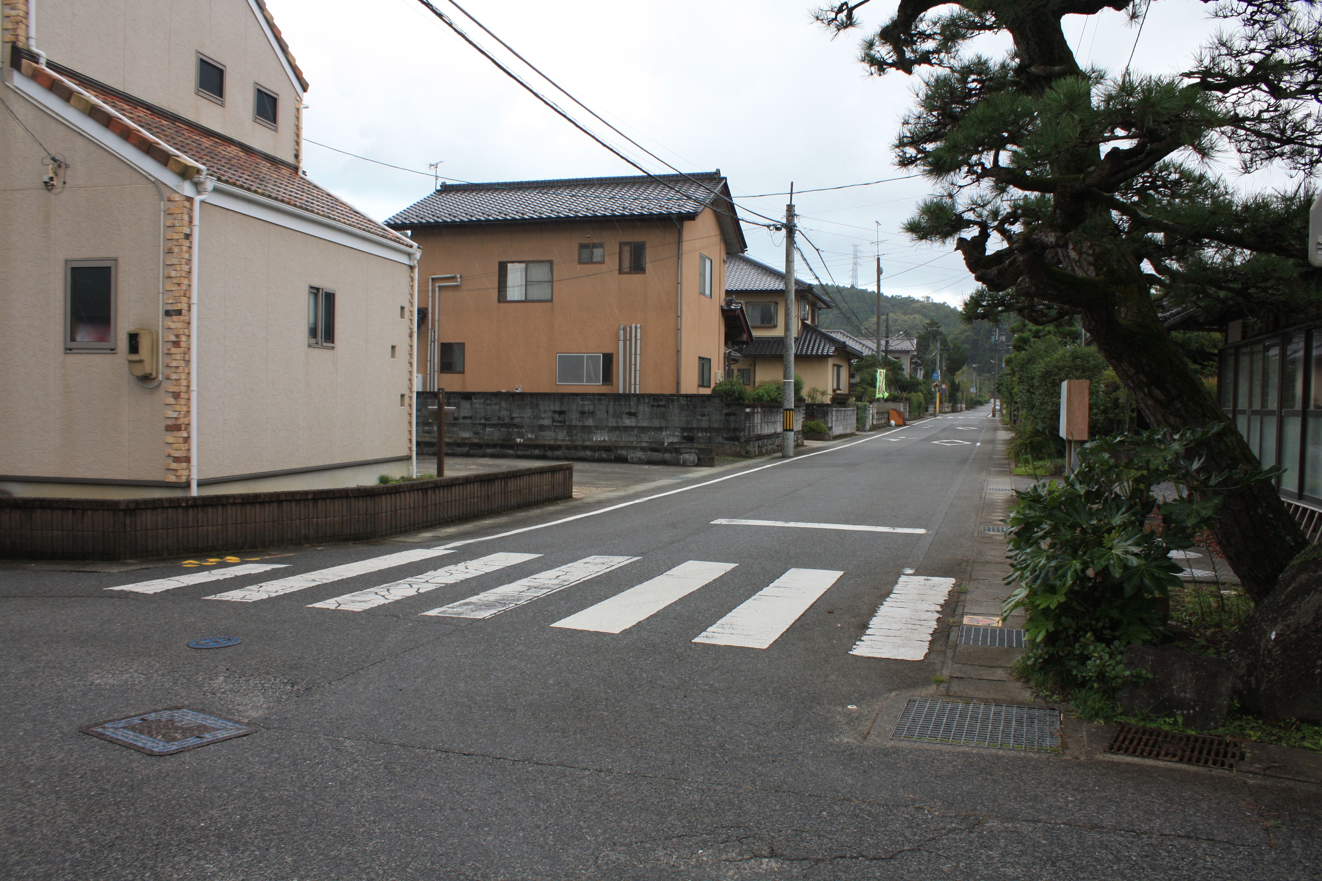 ■写真2-2 渡辺公民館入口から南方を見る　写真左に見えるのは旧「角屋」があった跡　(令和3年9月　小宅幸一撮影)