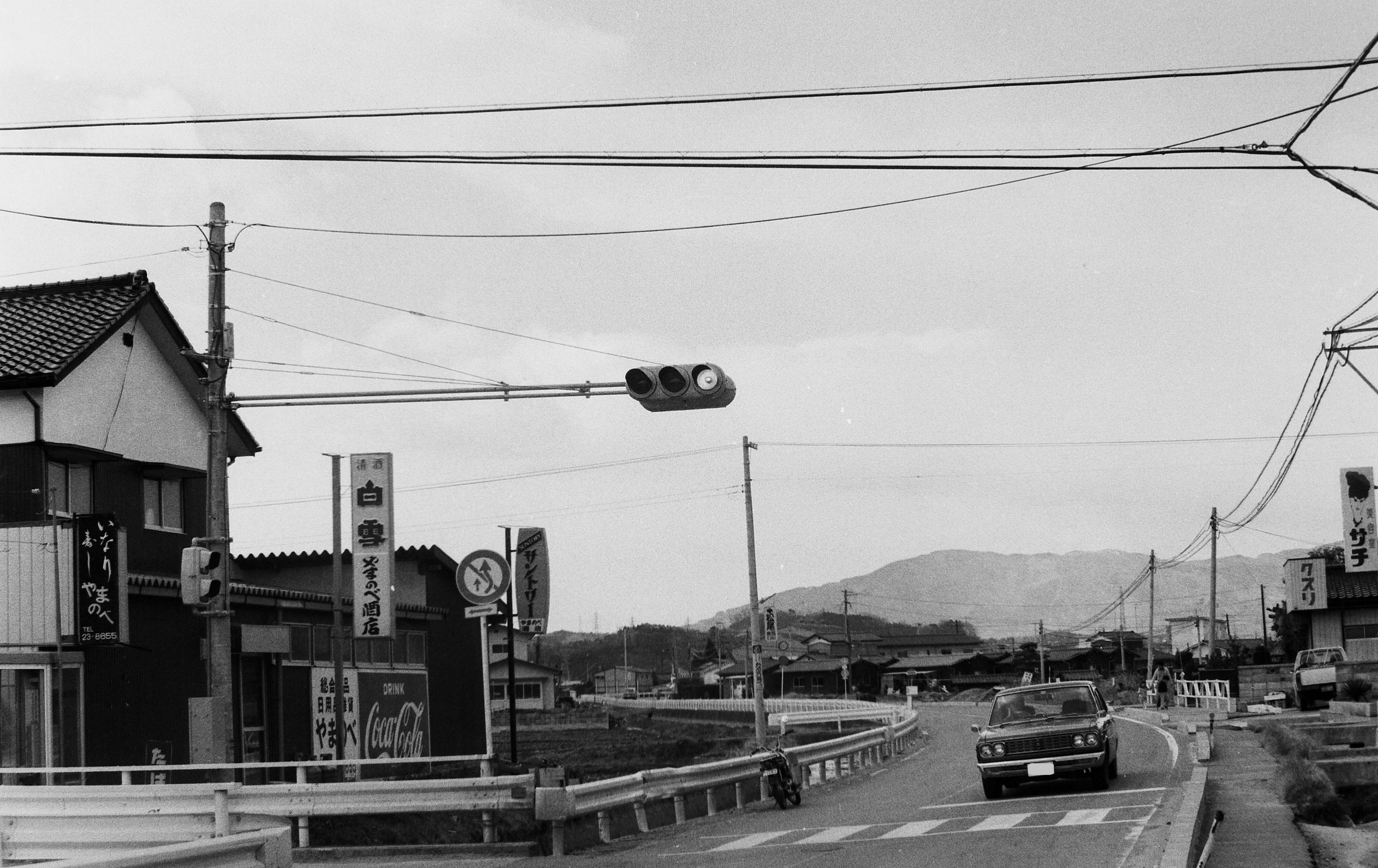 4.■写真1-1　平北白土の市営宮田団地入口　写真右方では夏井川後背の微高地に位置し、昔からの家々が散在していた。写真左側は、水田を埋めて建設された市営宮田団地に通じる。　〔昭和53(1978)年4月　いわき民報社撮影〕