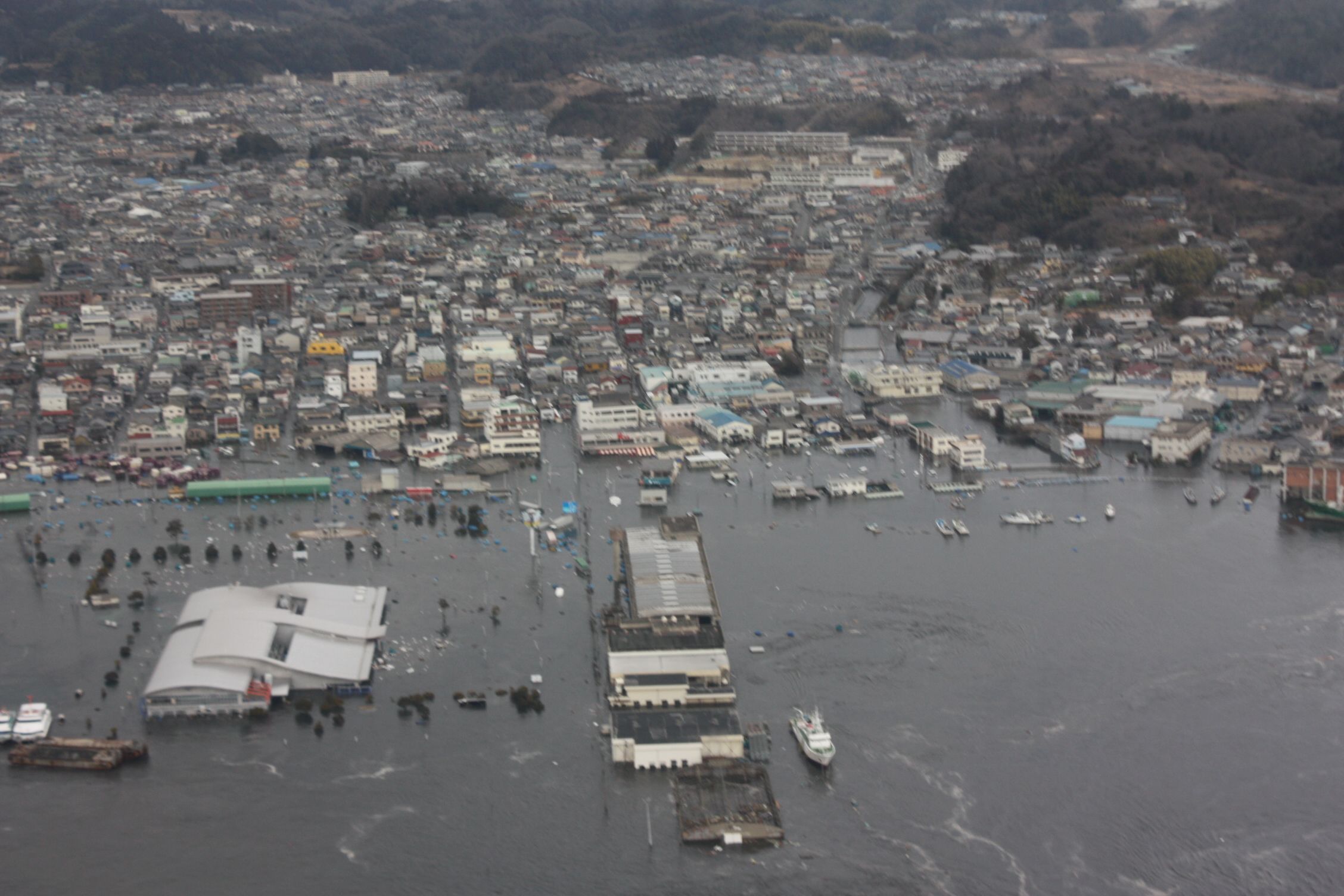 ■6・小名浜写真2-3  東北地方太平洋沖地震(東日本大震災)に起因する大津波に襲われる小名浜港湾を南側から見る　大津波が押し寄せ、埠頭では「いわきら・ら・ミュウ」と「アクアマリンふくしま」の屋根部分が見えるだけ。　〔平成23(2011)年3月11日午後3時50分　福島県消防防災航空隊撮影